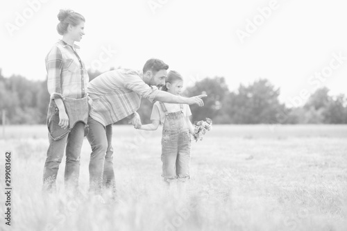 Young Caucasian family walking across field with young girl holding bouquet of flowers, man is pointing to the distance