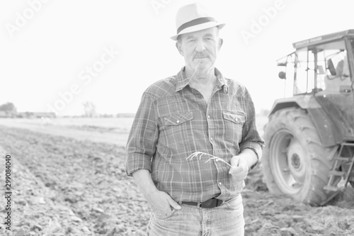Black and white photo of senior farmer standing against tractor in field