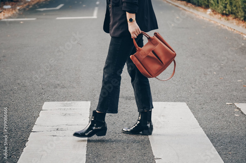 fashion blogger autumn 2019 outfit details. fashionable woman wearing black jeans, black ankle shoes a brown tan trendy leather handbag. crossing the street. detail of a perfect fall fashion outfit.  photo