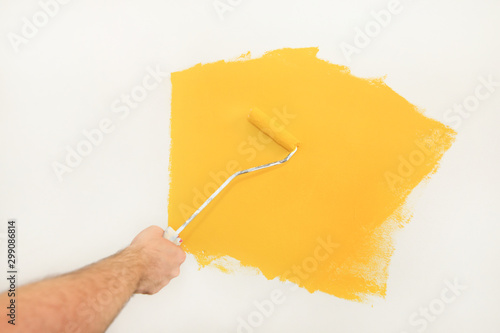 Construction worker and handyman doing finish renovation at apartment. Professional painter using paint roller brush painting of wall with yellow color on construction site. Home renovation concept.