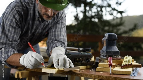 Adult carpenter craftsman wearing helmet and leather protective gloves, with a pencil and the carpenter's square trace the cutting line on a wooden table. Construction industry, housework do it yourse photo