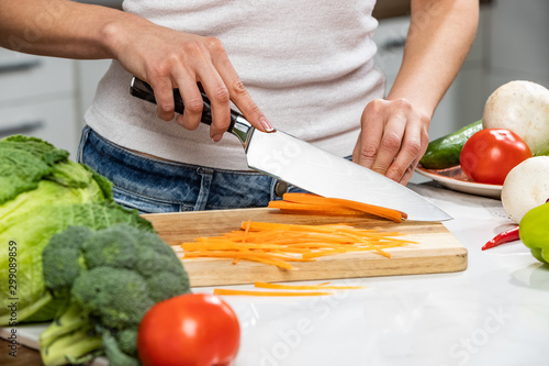 Close up of woman's hands cooking in the kitchen. Housewife slicing fresh carrot. Vegetarian and healthily cooking concept