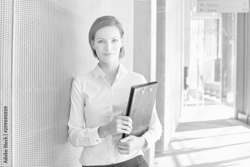 Black and white photo of businesswoman leaning on wall while holding document Black and white photo of businesswoman leaning on wall while holding document