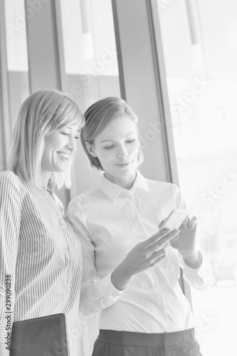 Black and white photo of businesswoman showing smartphone to colleague in office