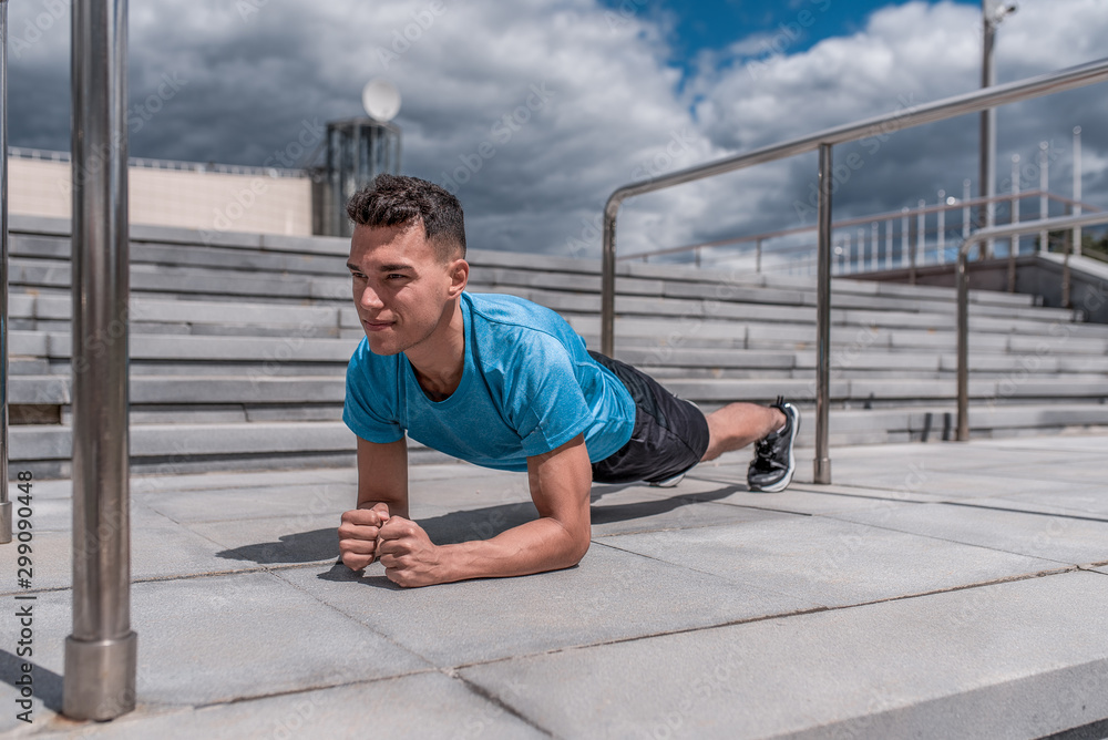 Athletic man, standing in bar, training abs and back muscles, training in summer day in city, an active lifestyle, modern fitness workout, sportswear t-shirt, shorts, sneakers.