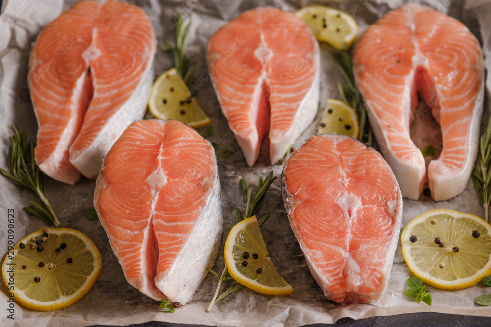Raw, fresh salmon steaks on a baking tray with lemon, rosemary and cherry tomatoes. Raw salmon, red fish. Cooking salmon, seafood. Healthy eating concept. Salmon and spices Raw, fresh salmon steaks on a baking tray with lemon, rosemary and cherry tomatoes. Raw salmon, red fish. Cooking salmon, seafood. Healthy eating concept. Salmon and spices