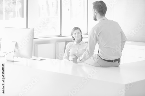 Black and white photo of businessman sitting on table while talking to receptionist in office lobby during break
