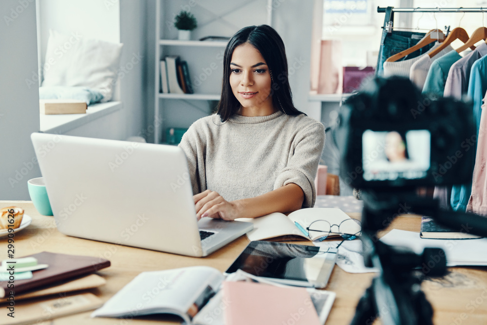 Beautiful young woman in casual clothing making social media video while using laptop at home Beautiful young woman in casual clothing making social media video while using laptop at home