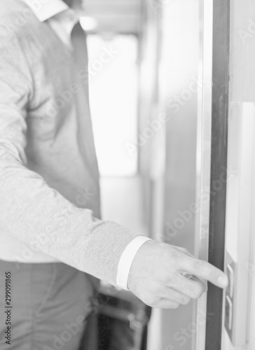 Black and white photo of businessman pressing button while waiting for elvator