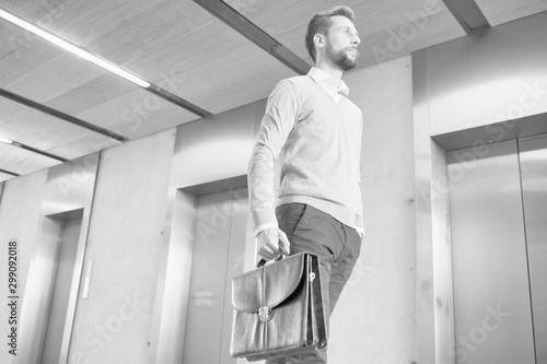 Black and white photo of confident businessman walking against elevator in office