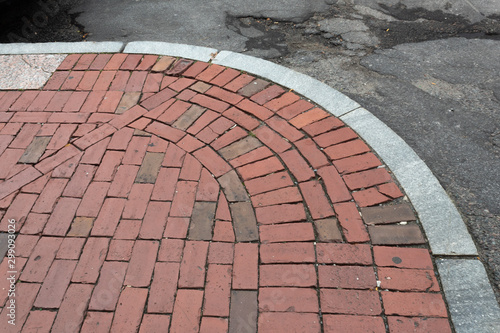 Old brick sidewalk bordered with granite alongside crumbling asphalt street, horizontal aspect