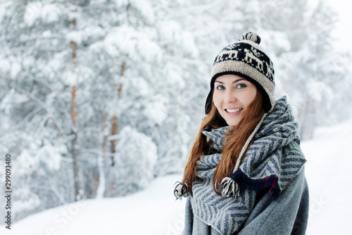 Beautiful young woman standing among snowy trees in winter forest and enjoying snow.