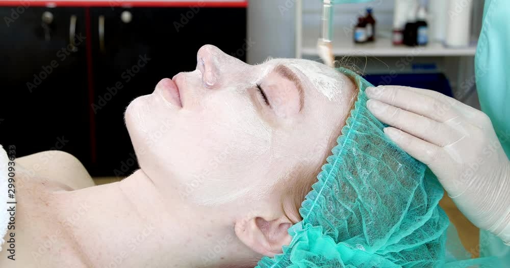 Cosmetologist applying mask onto woman's face in salon Cosmetologist applying mask onto woman's face in salon