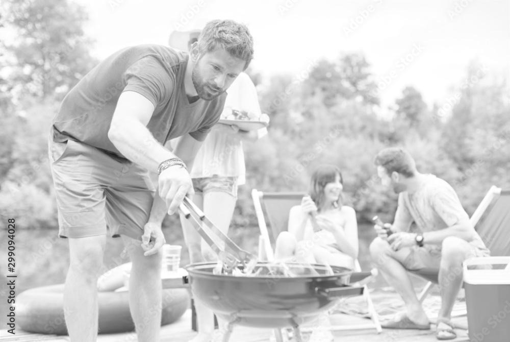 Man using bellows for preparing food in barbecue grill with friends on pier Man using bellows for preparing food in barbecue grill with friends on pier