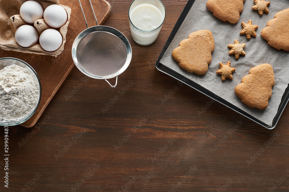 top view of Christmas cookies on oven tray near ingredients on wooden table