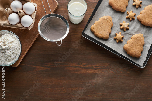 top view of Christmas cookies on oven tray near ingredients on wooden table