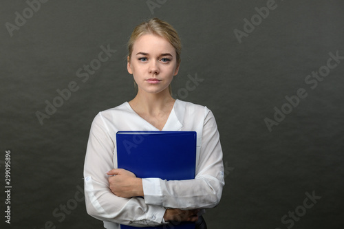 Portrait of young beautiful blonde businesswoman holding blue folder on grey background.