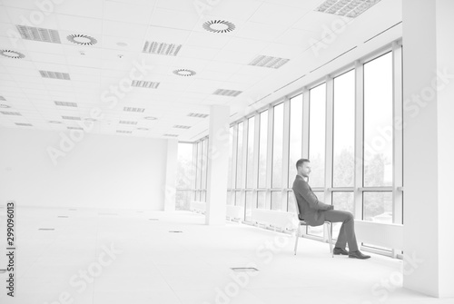 Full length of thoughtful young businessman sitting on chair while looking through window at new empty office