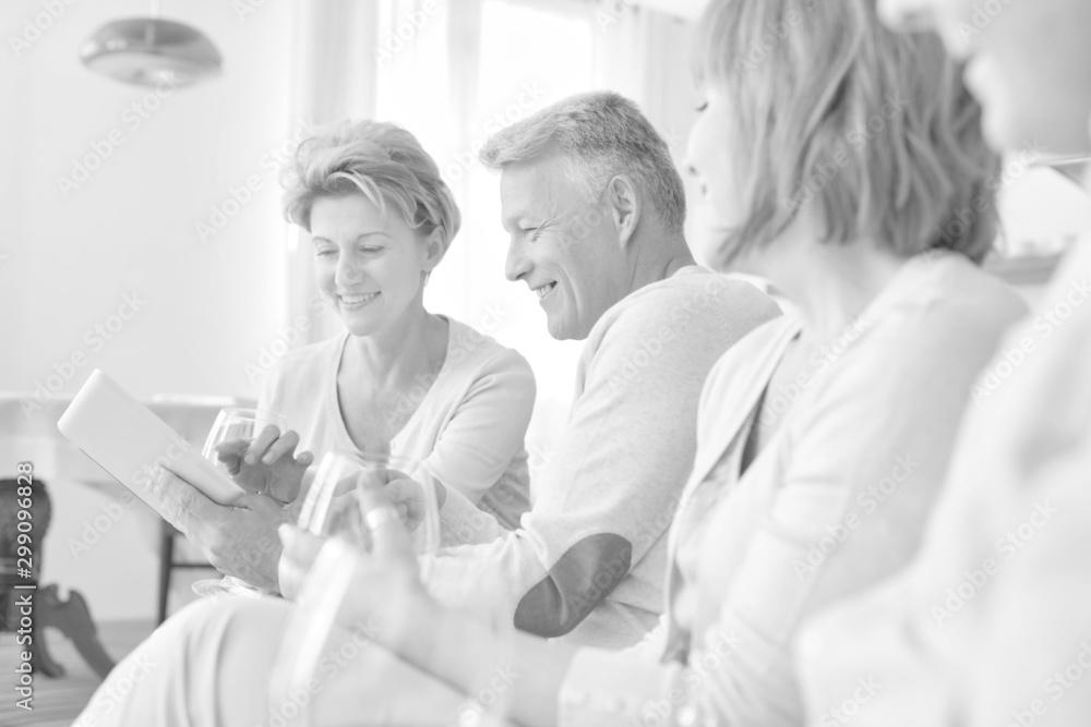 Fototapeta premium Smiling mature man holding digital tablet while sitting with friends at home