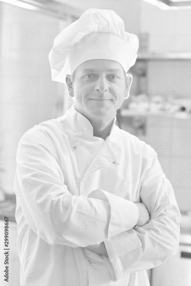 Black and white photo of  confident mature chef standing with arms crossed in kitchen at restaurant