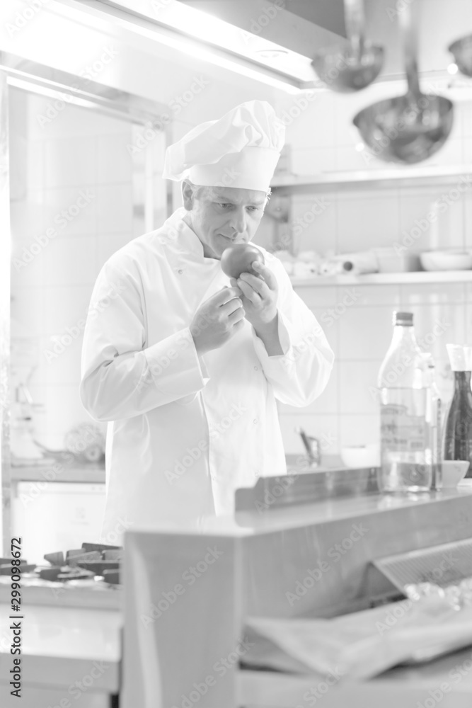 Black and white photo of Mature chef smelling fresh red tomato while standing at restaurant kitchen Black and white photo of Mature chef smelling fresh red tomato while standing at restaurant kitchen