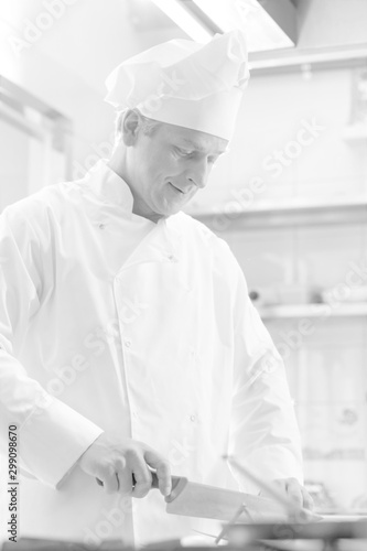 Black and white photo of confident mature chef cutting vegetables in kitchen
