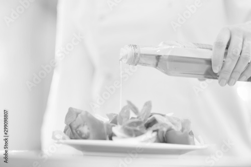 Black and white photo of Smiling mature chef pouring oil on salad in plate at restaurant