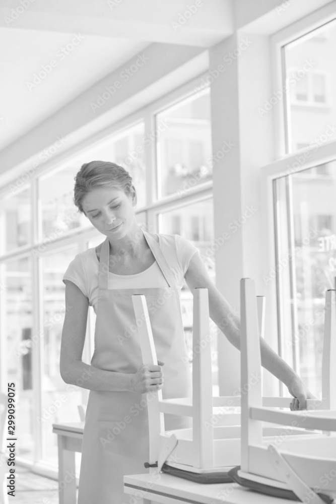 Black and white photo of Young waitress arranging chair and table at restaurant Black and white photo of Young waitress arranging chair and table at restaurant