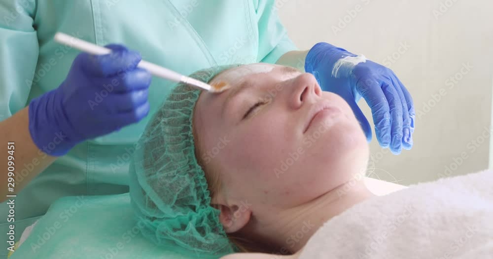 Cosmetologist applying mask onto woman's face in salon Cosmetologist applying mask onto woman's face in salon