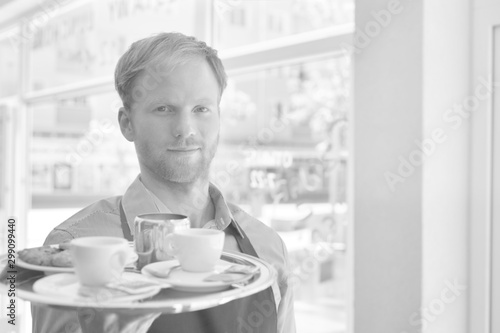 Young waiter serving coffee and cookies at restaurant