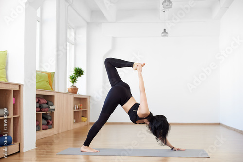Advanced yoga. Young slender brunette woman in yoga class training stretching and exercises. Side view of girl doing One-legged downward-facing dog pose. Healthy lifestyle in moder fitness club