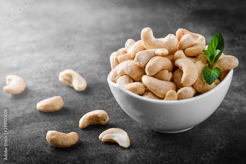 Cashew nuts in white porcelain bowl on dark stone table. Delicacies nut on black background.