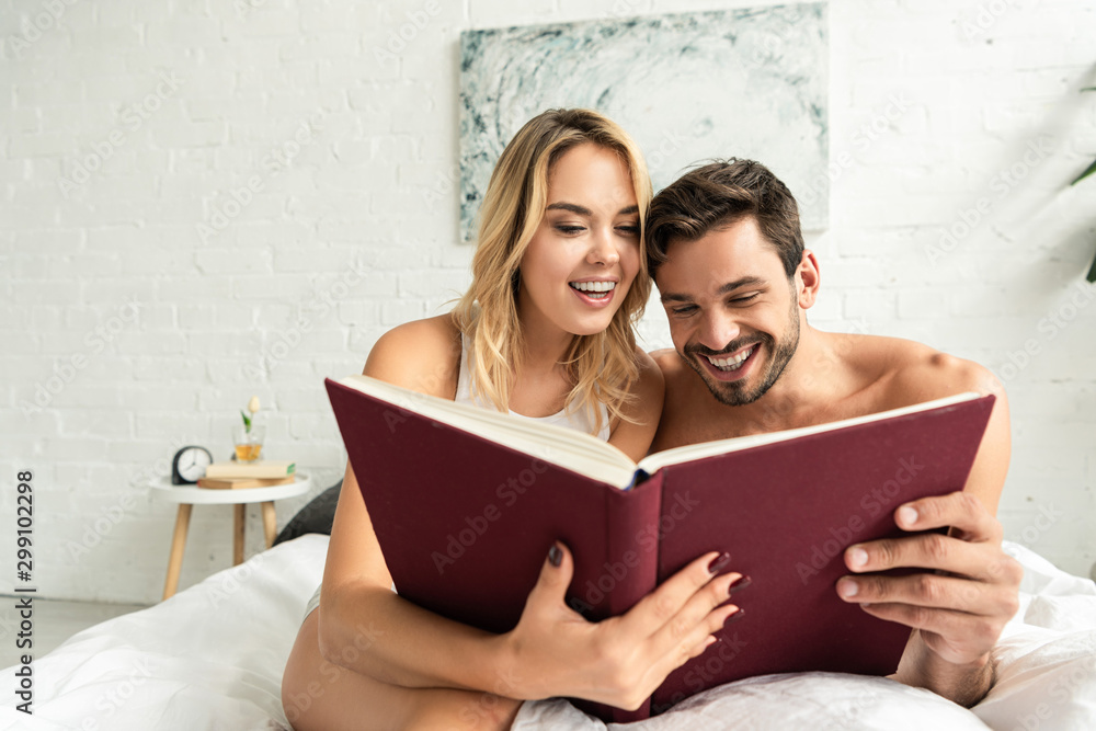 cheerful couple reading book together in bed in the morning
