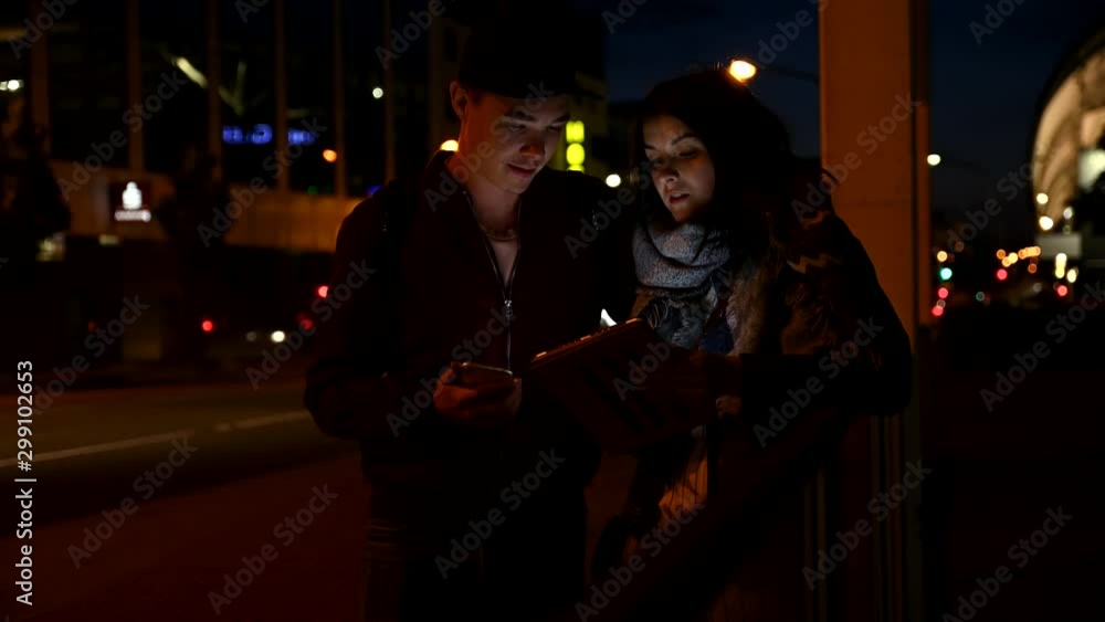 Couple using tablet and smartphone on the street at night Couple using tablet and smartphone on the street at night