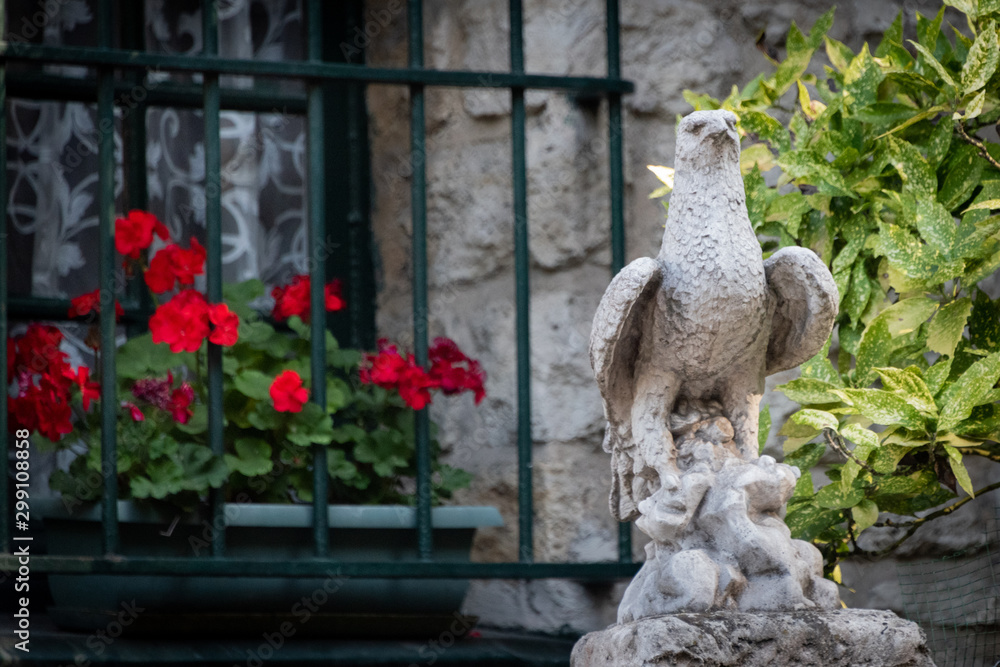 Obraz premium stone sculpture of a hawk with barred window and red geraniums in background