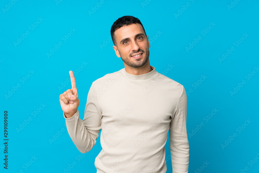 Young man over isolated blue background showing and lifting a finger in sign of the best Young man over isolated blue background showing and lifting a finger in sign of the best