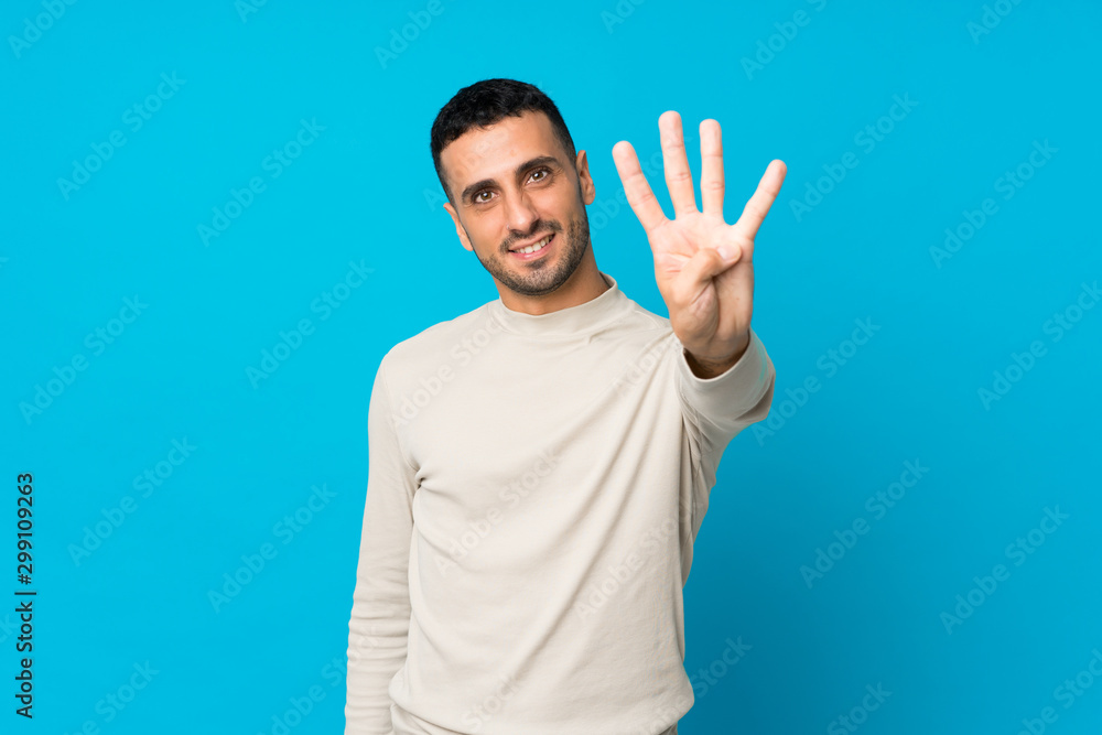 Naklejka premium Young man over isolated blue background happy and counting four with fingers
