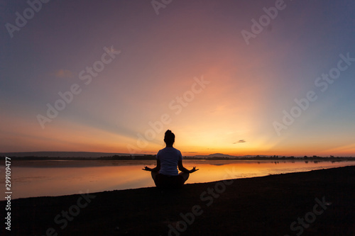 Young woman in a meditating yoga pose overlooking the beautiful sunset. Mind body spirit concept.