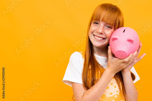 schoolgirl on an orange background hugs a piggy bank in the form of a pink pig