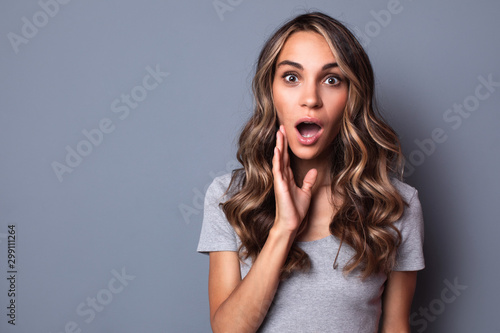 Closeup portrait of a beautiful surprised woman with hairstyle on gray background.