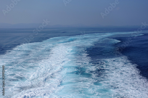 Large white waves generated from high speed boat in deep blue Aegean sea and sky