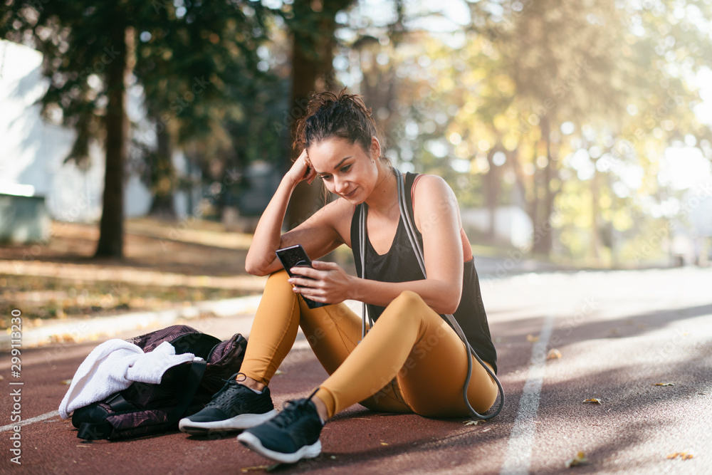 Young fitness woman in park. Athletic woman sitting on running track and  using phone. Stock Photo