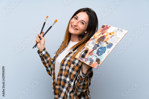 Young painter woman over isolated blue background