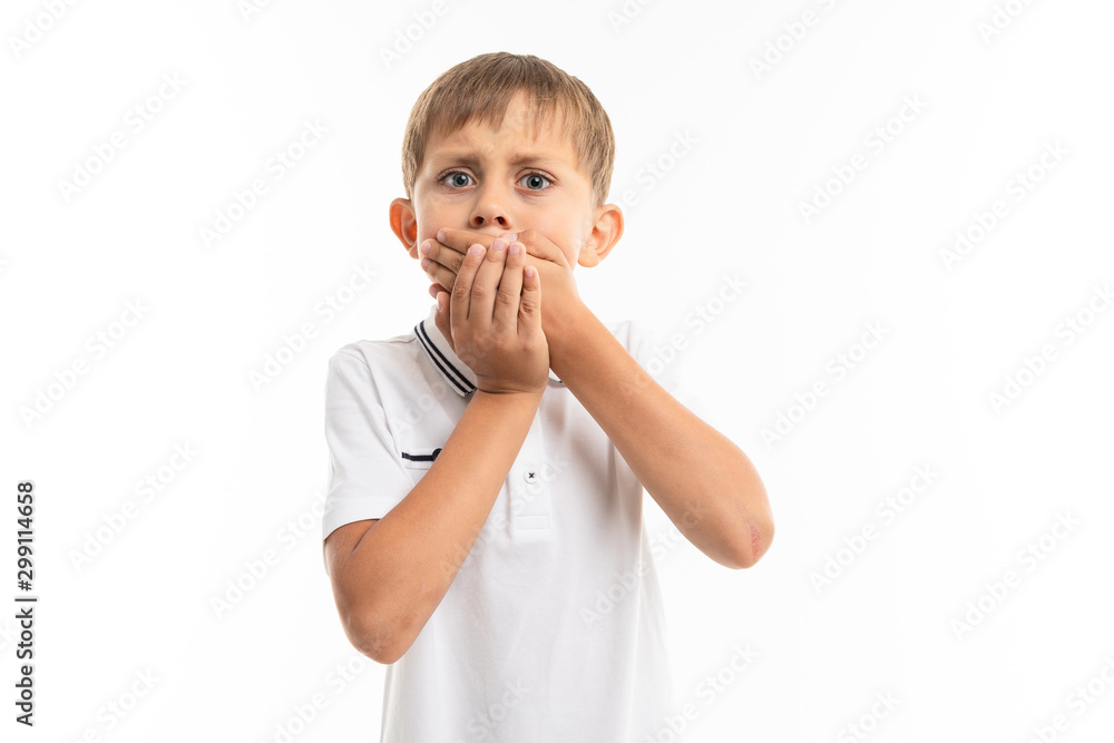 schoolboy on a white background closes his mouth with his hands, is afraid to blurt out, emotional portrait schoolboy on a white background closes his mouth with his hands, is afraid to blurt out, emotional portrait