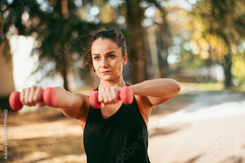 Beautiful woman working out outdoors. Sporty woman training on athletics track with dumbbells. 