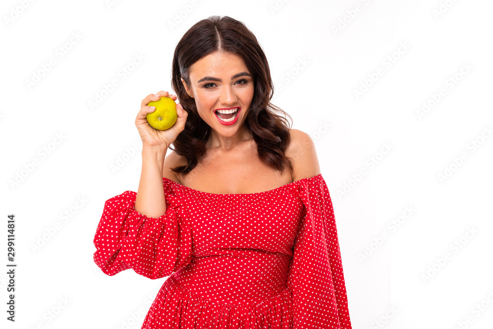 brunette with smooth beautiful teeth holds an apple in her hand, sexy girl in a red dress on a white background, healthy teeth, emotional portrait brunette with smooth beautiful teeth holds an apple in her hand, sexy girl in a red dress on a white background, healthy teeth, emotional portrait