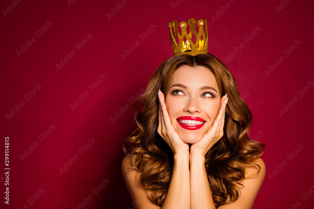 Photo of pretty model lady red pomade nude shoulders golden crown on head arms cheekbones looking empty space isolated burgundy color background Photo of pretty model lady red pomade nude shoulders golden crown on head arms cheekbones looking empty space isolated burgundy color background