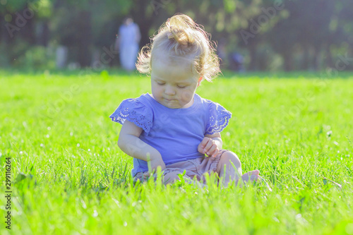 Cute little girl sits on the green grass, outdoors, summer time, blurred background