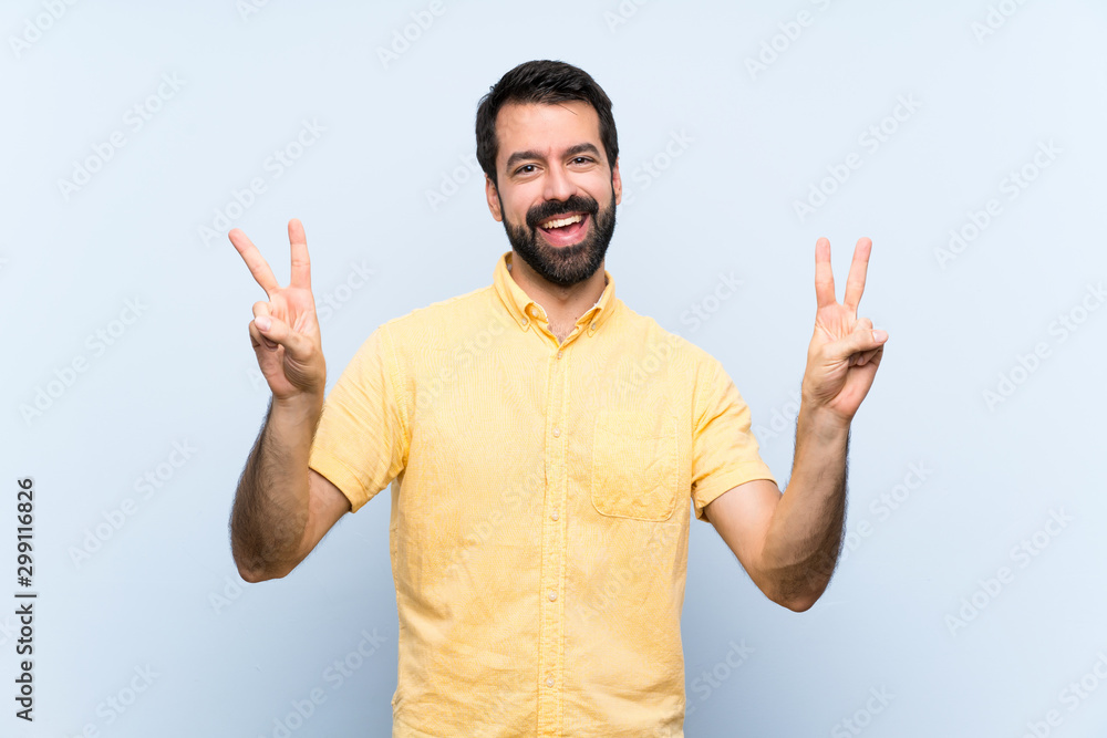Naklejka premium Young man with beard over isolated blue background showing victory sign with both hands
