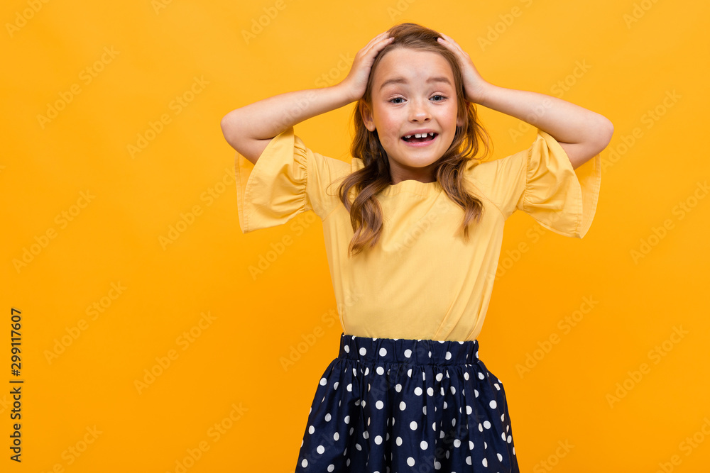 beautiful girl holds her head with hands on a background of an orange wall, emotional portrait